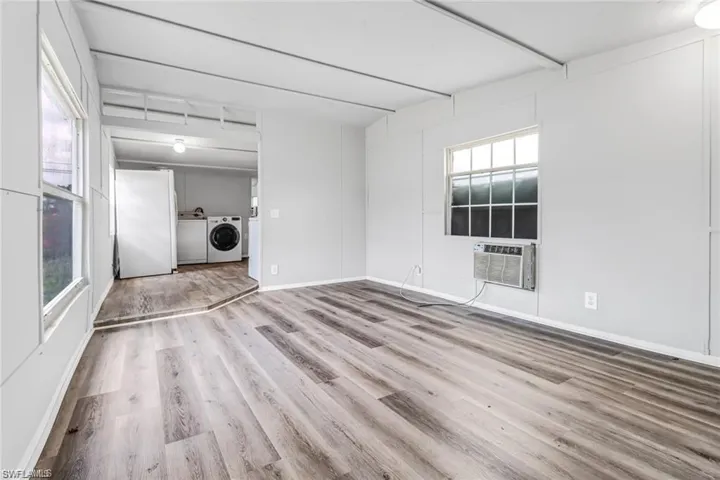 Unfurnished room featuring light wood-type flooring, plenty of natural light, washing machine and dryer, and cooling unit