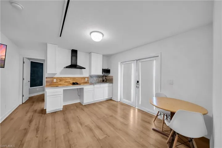 Kitchen featuring white cabinetry, light countertops, wall chimney range hood, light wood-type flooring, and backsplash
