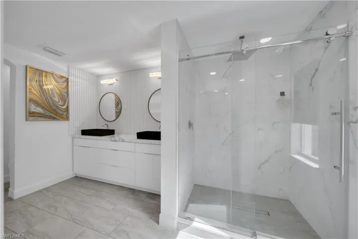 Full bathroom featuring vanity, a marble finish shower, and light marble finish flooring
