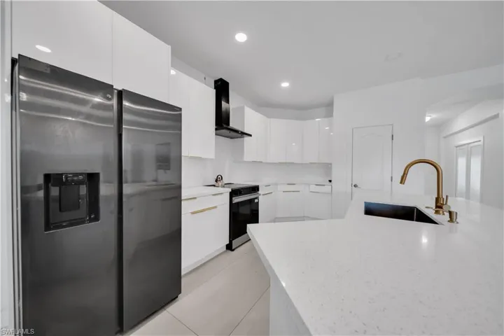 Kitchen featuring refrigerator with ice dispenser, modern cabinets, wall chimney exhaust hood, white cabinetry, and black range with electric cooktop