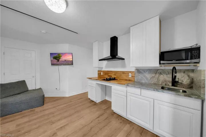 Kitchen with white cabinetry, stainless steel microwave, wall chimney exhaust hood, and tasteful backsplash