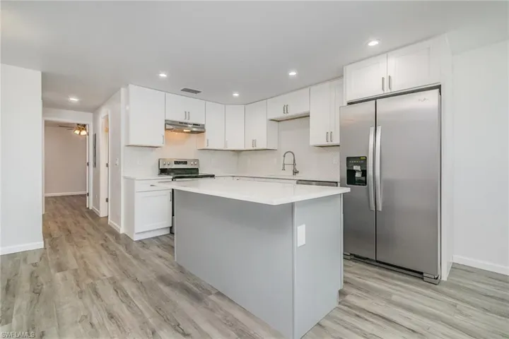 Dual tone kitchen featuring stainless steel appliances, a kitchen island, light wood-type flooring, recessed lighting, and decorative backsplash