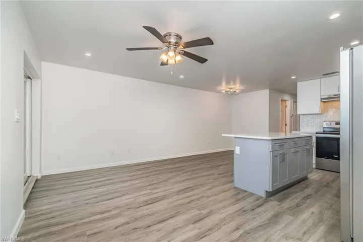 Two tone kitchen with stainless steel appliances, ceiling fan, a kitchen island, light wood-type flooring, and recessed lighting