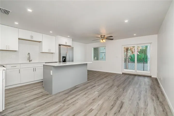 Dual tone kitchen featuring stainless steel refrigerator with ice dispenser, a kitchen island, light wood-style floors, ceiling fan, and recessed lighting