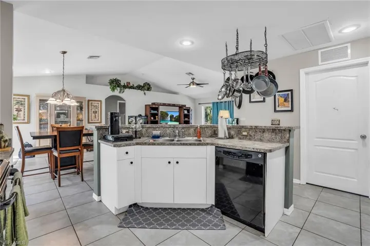 Kitchen featuring light tile patterned floors, white cabinets, dishwasher, ceiling fan, and vaulted ceiling
