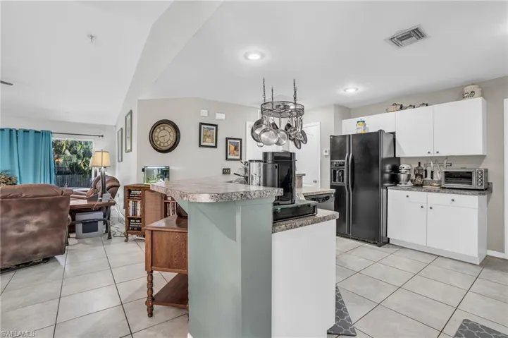 Kitchen featuring white cabinetry, lofted ceiling, light tile patterned floors, and black refrigerator with ice dispenser