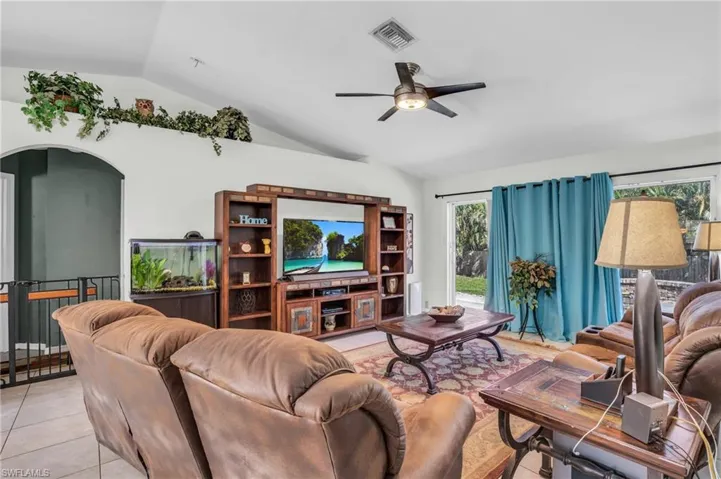 Tiled living room with ceiling fan and lofted ceiling