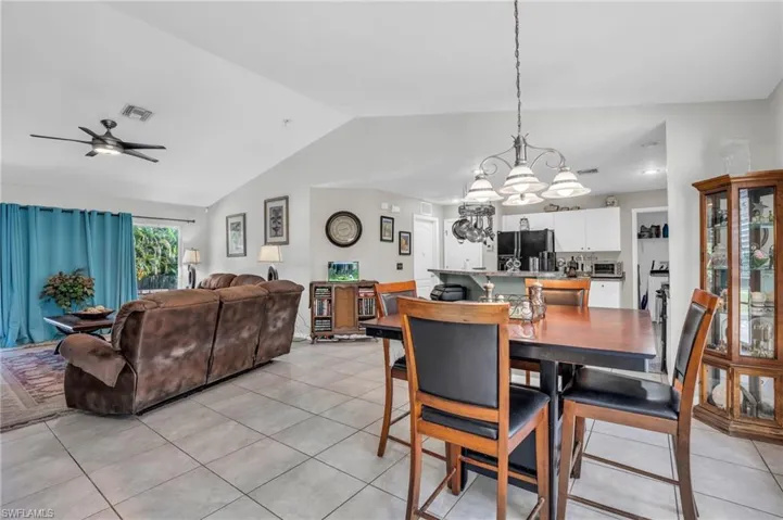 Tiled dining space with ceiling fan with notable chandelier and vaulted ceiling