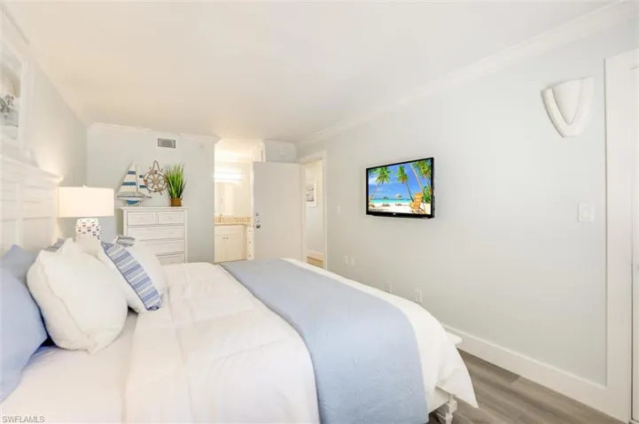 Bedroom featuring wood finished floors, crown molding, and ensuite bath
