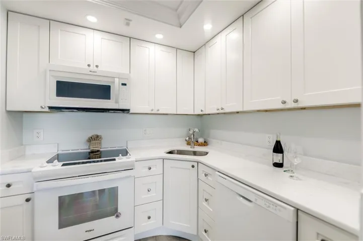 Kitchen with white appliances, white cabinets, recessed lighting, light stone countertops, and ornamental molding