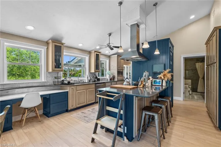 Kitchen with glass insert cabinets, a breakfast bar, an island with sink, blue cabinetry, and island range hood