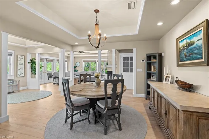 Dining room with light wood-style flooring, recessed lighting, decorative columns, a chandelier, and a raised ceiling