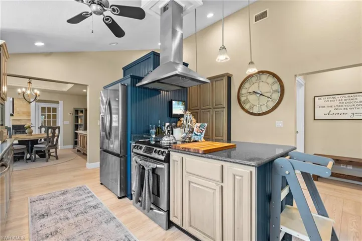 Kitchen featuring pendant lighting, island exhaust hood, stainless steel appliances, ceiling fan, and lofted ceiling