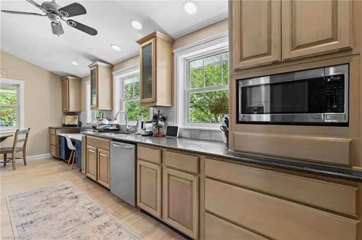 Kitchen with stainless steel appliances, glass insert cabinets, light wood-style floors, a ceiling fan, and vaulted ceiling