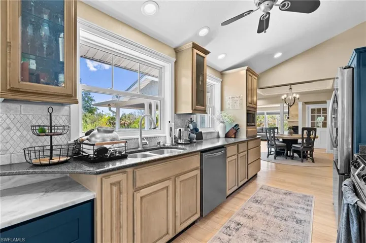 Kitchen with glass insert cabinets, light wood finished floors, dark stone countertops, a ceiling fan, and appliances with stainless steel finishes