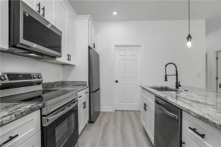 Kitchen featuring appliances with stainless steel finishes, light wood finished floors, light stone counters, white cabinets, and hanging light fixtures