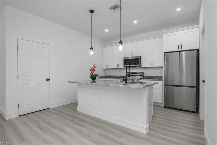 Kitchen featuring stainless steel appliances, light wood-type flooring, white cabinetry, an island with sink, and recessed lighting