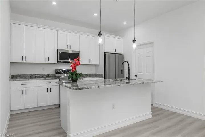 Kitchen with stainless steel appliances, a center island with sink, white cabinets, light wood-type flooring, and stone countertops