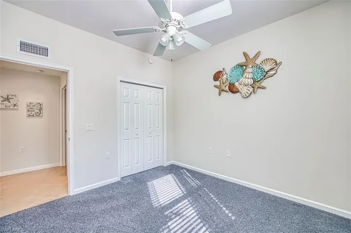 Unfurnished bedroom with carpet, a ceiling fan, a closet, and tile patterned floors