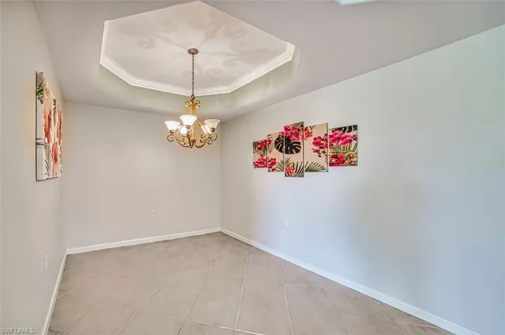 Spare room with crown molding, a tray ceiling, and a chandelier