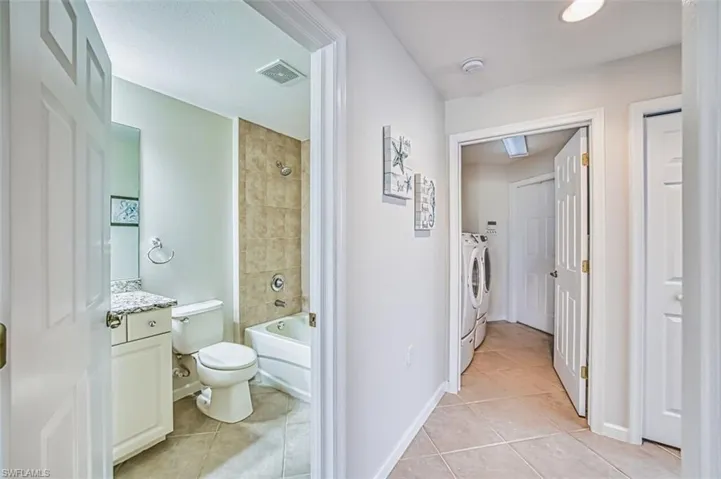Bathroom featuring washtub / shower combination, light tile patterned floors, vanity, and washing machine and dryer