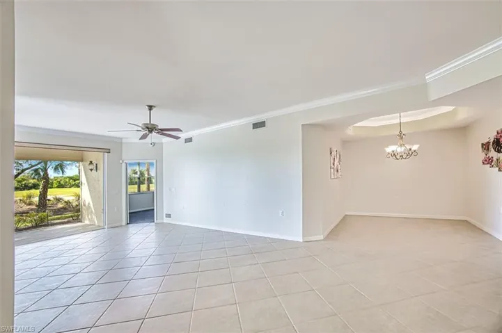 Empty room featuring light tile patterned flooring, ceiling fan, and a chandelier