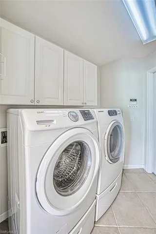 Laundry area featuring light tile patterned floors, cabinet space, and washing machine and clothes dryer