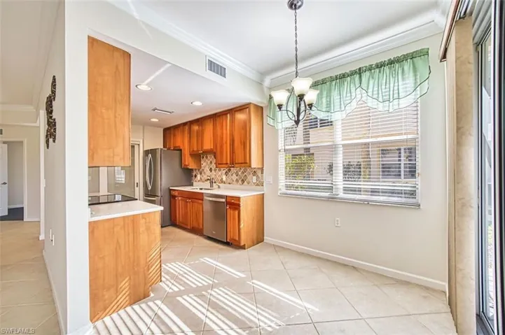 Kitchen with ornamental molding, light tile patterned floors, light countertops, a chandelier, and brown cabinets