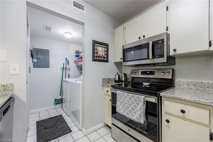 Kitchen featuring light tile patterned floors, stainless steel appliances, electric panel, a textured ceiling, and washing machine and clothes dryer