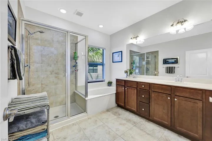 Bathroom featuring a stall shower, double vanity, a garden tub, and light tile patterned floors