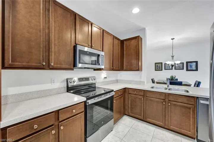 Kitchen with stainless steel appliances, light countertops, hanging lights, light tile patterned flooring, and wood finish cabinetry