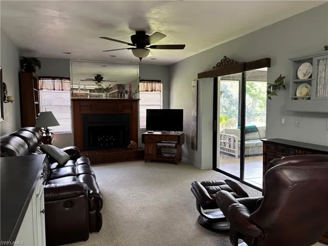 Living area featuring a fireplace with a wood mantle and brick hearth, ceiling fan, and carpet flooring