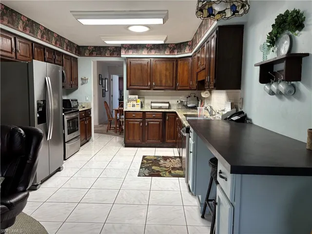 Kitchen featuring wood cabinetry, stainless steel appliances, white tile flooring, and a breakfast bar with dark countertops