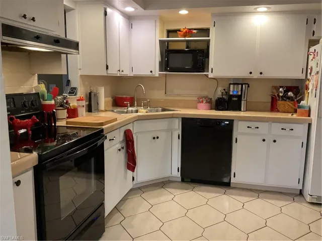 Kitchen with stove, dishwasher, white cabinetry, light floors, and exhaust hood