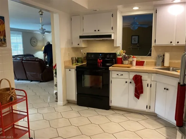 Kitchen with a ceiling fan, black electric range, white cabinetry, and tile counters