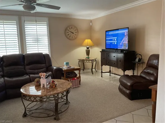 Living area with ornamental molding, light tile patterned floors, ceiling fan, and light colored carpet