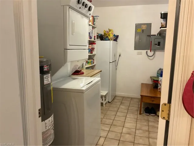 Laundry room with light tile patterned floors, electric panel, stacked washer / dryer, and water heater