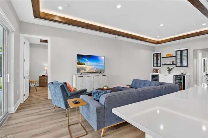 Living area featuring recessed lighting, light wood-type flooring, a bar, beverage cooler, and a raised ceiling