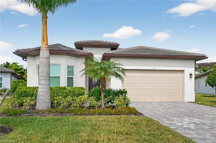 View of front facade featuring a tile roof, stucco siding, decorative driveway, and an attached garage