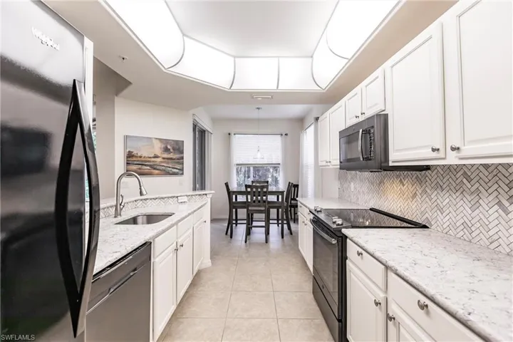 Kitchen featuring tasteful backsplash, white cabinets, black appliances, and sink