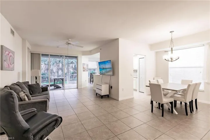 Living room with ceiling fan with notable chandelier and light tile patterned flooring