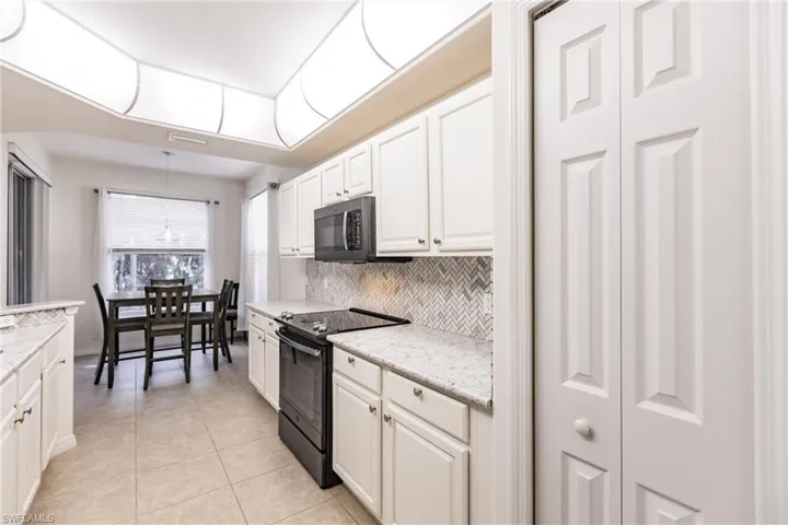 Kitchen with light stone countertops, decorative backsplash, white cabinets, black range with electric cooktop, and light tile patterned floors