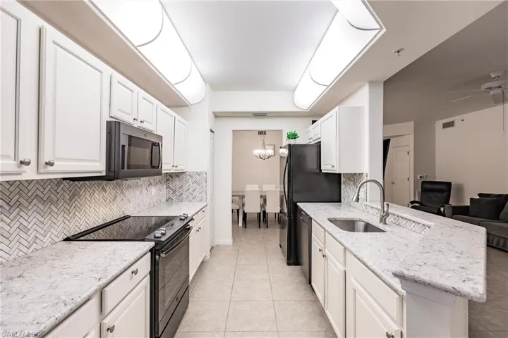 Kitchen with white cabinets, backsplash, sink, and black appliances