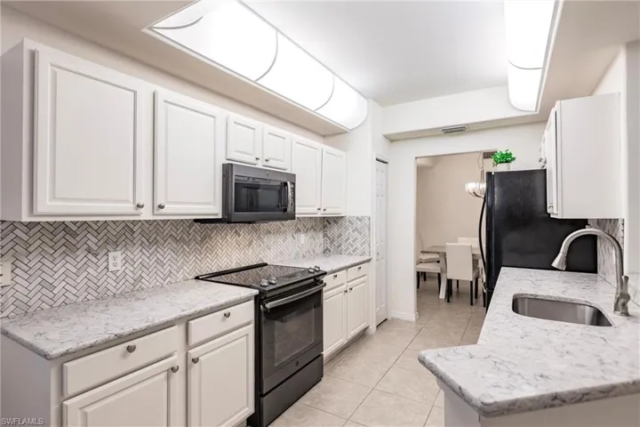 Kitchen with white cabinets, sink, decorative backsplash, and black appliances