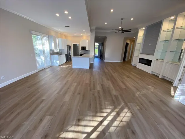 Unfurnished living room with light wood-type flooring, crown molding, ceiling fan, recessed lighting, and a large fireplace