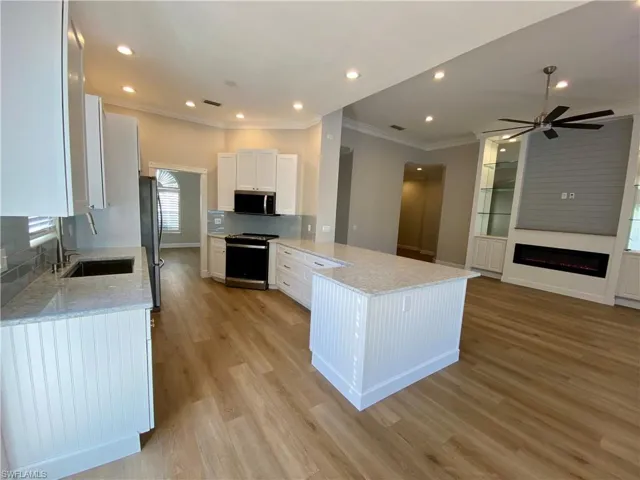 Kitchen with light stone countertops, white cabinets, stainless steel appliances, a peninsula, and open floor plan