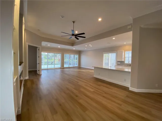 Unfurnished living room featuring crown molding, a ceiling fan, light wood-style floors, recessed lighting, and a raised ceiling