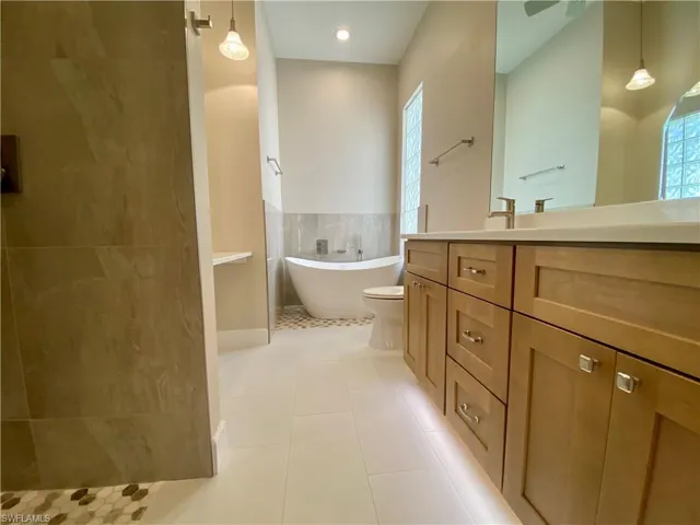Bathroom with vanity, a freestanding bath, a walk in shower, and light tile patterned flooring