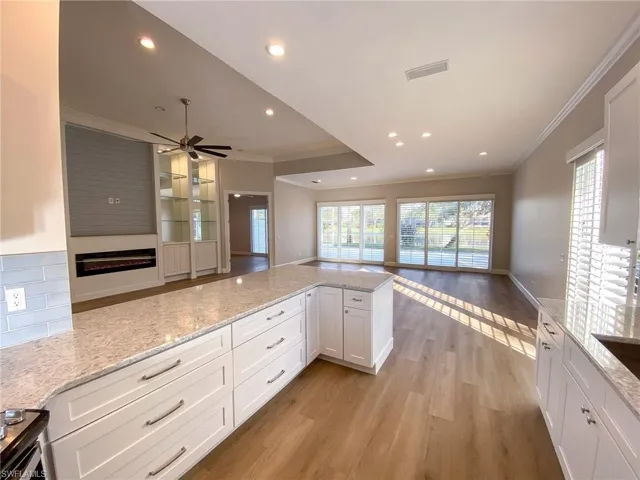 Kitchen with open floor plan, white cabinetry, light stone countertops, crown molding, and light wood-style floors