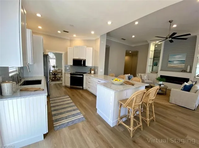 Kitchen featuring light stone countertops, a peninsula, white cabinetry, a breakfast bar area, and ornamental molding